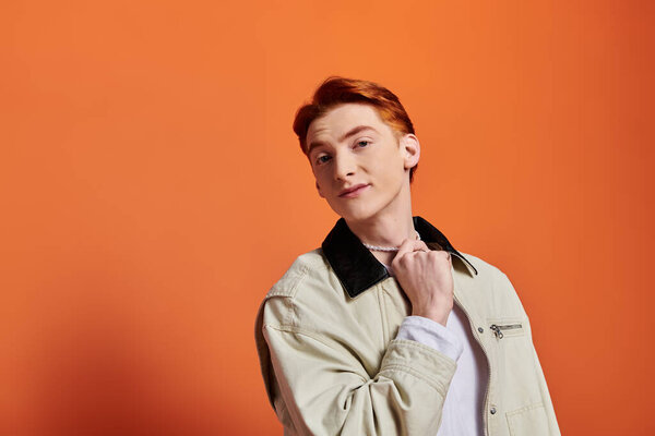 Красивый молодой человек демонстрирует свои эмоции, задумчиво позируя на яркой оранжевой стене..