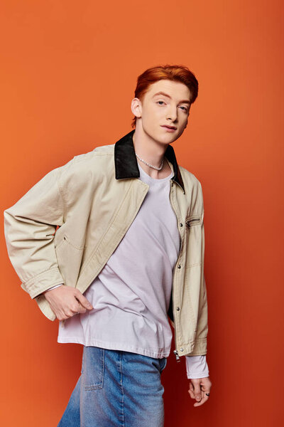 A young and handsome man stands confidently against an orange wall, expressing deep emotions.