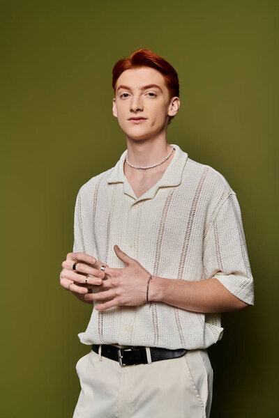 A stylish young man shows emotions in his trendy outfit against a vibrant green background.