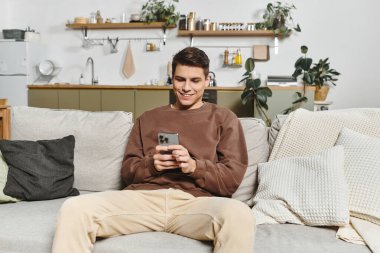 Relaxation takes center stage as a young man enjoys his smartphone in a warm living space. clipart