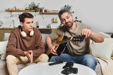 Genç bir çocuk sıcak bir yaşam alanında dikkatlice dinlerken bir adam gitarını akort eder..