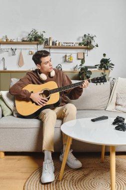 Genç bir adam, bitki ve dekorla dolu bir salonda rahat bir kanepede gitar çalıyor..