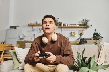 A young man enjoys a thrilling game at home while wearing headphones and focused on their screen. clipart