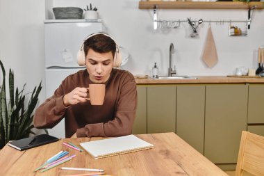 Sıcak bir içki yudumlarken, bir adam masada oturur, evde yaratıcı bir öğleden sonraya hazırdır..