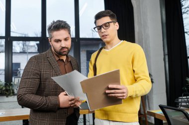 İki profesyonel, ilk iş gününde canlı bir ofiste gerekli belgeleri tartışıyor..