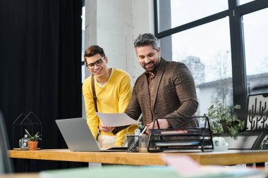 Colleagues share a joyful moment while discussing tasks at a modern office workstation. clipart