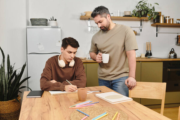 A young man writes in a notebook while a caring companion supports him at home.