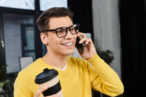 Young professional chats on the phone while holding a coffee cup in a welcoming workspace.