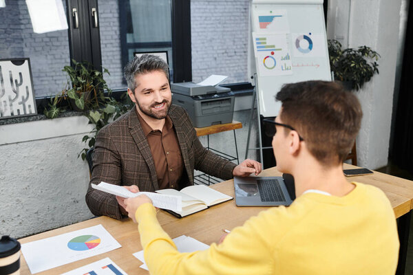 Two professionals interact in a welcoming office environment, sharing insights and materials.