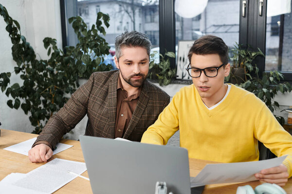 Two colleagues participate in onboarding, exchanging ideas while reviewing documents at a desk.