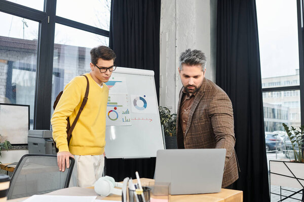 Two individuals collaborate at a desk, discussing plans while a presentation board stands nearby.