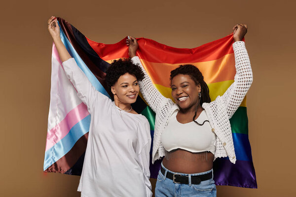 Two beautiful women proudly holding a rainbow flag, sharing joy and love in a trendy setting.