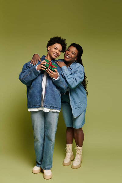 Two stylish women hug, displaying trendy outfits and bright smiles together.