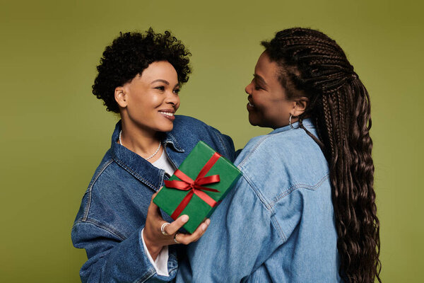 Две модно одетые женщины обнимаются с любовью, обмениваясь красочным подарком в яркой обстановке.