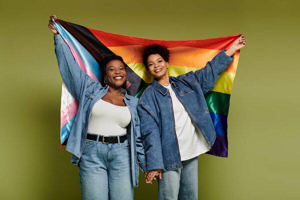 Две модные женщины держат красочный флаг гордости, излучающий любовь и счастье вместе.