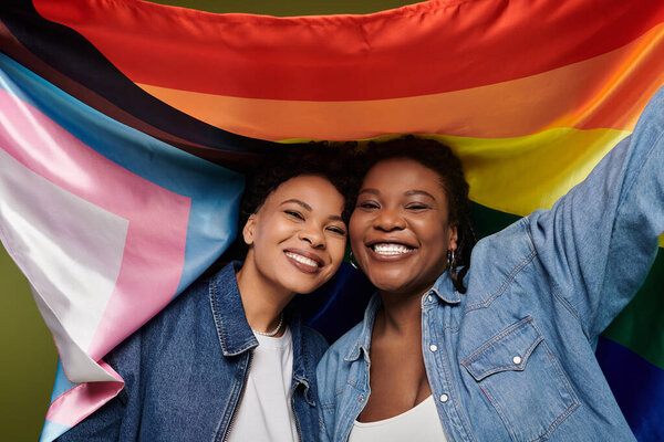 Joyful couple wraps in a rainbow flag, celebrating their love and identity.