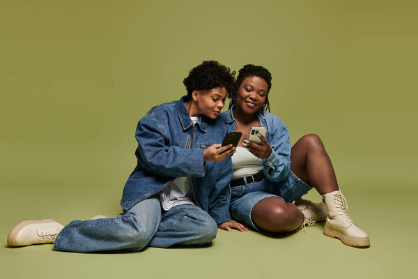 Две яркие женщины разделяют восхитительный момент, небрежно исследуя свои телефоны в модном наряде.