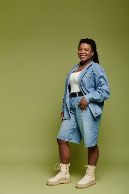 Canlı giyinmiş neşeli Afro-Amerikalı kadın yeşil zeytin arkaplanda poz veriyor..