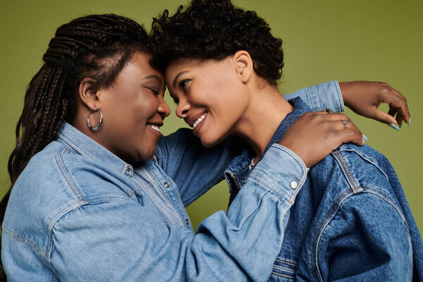 A stylish lesbian couple enjoys a tender moment against a vibrant backdrop.