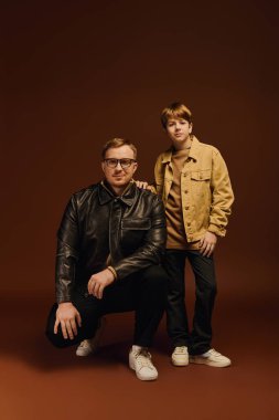 Baba ve oğul günlük kıyafetlerle gülümsüyor, stüdyoda birlikte güzel vakit geçiriyorlar..