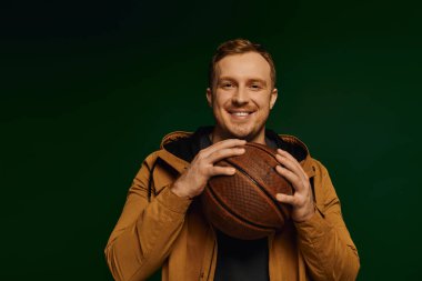 Günlük kıyafetli kendine güvenen bir adam yaratıcı stüdyo ortamında basketbol topuyla poz verir..