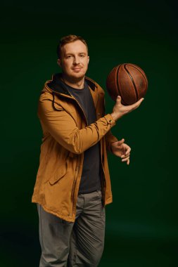 Yakışıklı bir adam, elinde basketbol topuyla bir stüdyoda rahat bir şekilde duruyor..