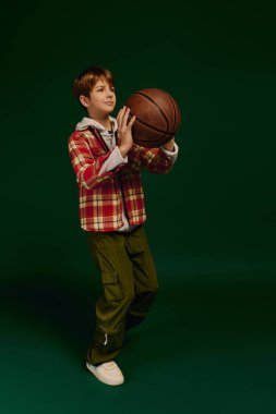 Genç bir çocuk, bir basketbol topuyla güven içinde poz verirken kareli kıyafetini gösteriyor..