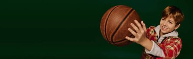 Genç bir çocuk sevinçle kareli bir kıyafetle poz veriyor, elinde basketbol topu, afiş.