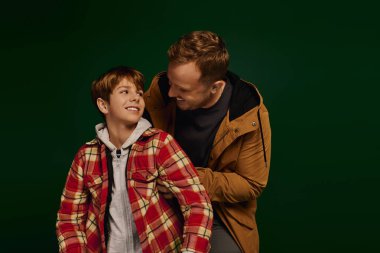 Baba ve oğul, bir stüdyo seansı sırasında şık günlük giysiler içinde neşeli bir gülümseme paylaşırlar..