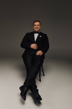 Çekici bir adam şık bir stüdyoda otururken smokin ve papyon giyer..