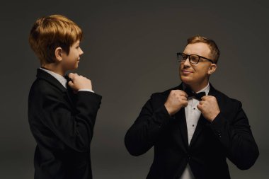 Handsome father and son dressed in matching tuxedos adjust their bow ties, exuding elegance. clipart