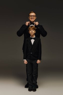 Yakışıklı bir baba, oğlunun papyonunu ayarlıyor ve aynı smokinleri bir stüdyoda sergiliyor..