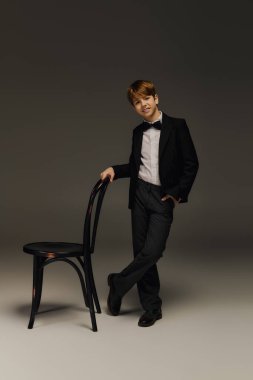 Papyonlu şık bir smokin giyen genç bir çocuk, stüdyoda güven içinde poz veriyor..