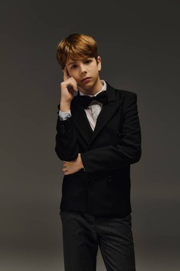 A preteen boy dressed in a sharp suit and bow tie strikes a confident pose in a studio. clipart