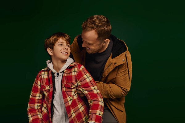 Отец и сын делятся радостными улыбками, одеваясь в стильные повседневные наряды во время студийной сессии.