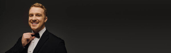 A stylish man in a tuxedo with a bow tie exudes confidence in a studio setting, banner