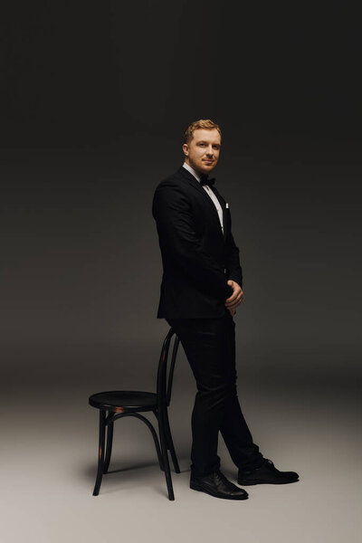 Красивый мужчина стоит в смокинге, демонстрируя классическую моду и уверенность в студии.