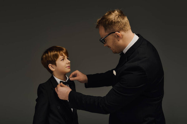 Красивый отец настраивает бабочку своего сына, оба элегантно одеты для особого случая.
