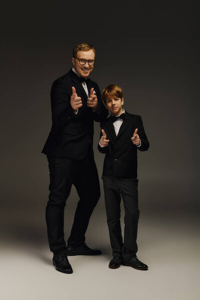 Классные отец и сын показывают свои стильные галстуки-бабочки и смокинги, излучающие очарование в студии.