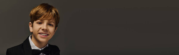 A preteen boy in a tuxedo smiles warmly, dressed elegantly for a special occasion in a studio, banner