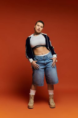 Genç bir kadın, koyu turuncu bir zemine karşı modern moda sergiliyor..