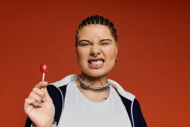 Parlak örgülü şık bir kadın elinde kırmızı bir lolipop tutarken neşeli bir şekilde gülümser..