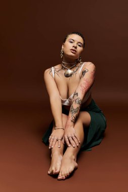 Kendine güveni tam bir kadın, sanatsal dövmelerini sıcak bir arkaplanda sergiliyor..