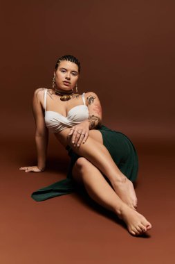 Genç ve şık bir kadın zarif bir şekilde kahverengi bir zemine yaslanır, özgüven ve beceri sergilerler..