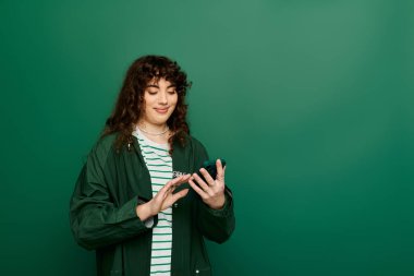 Kıvırcık saçlı genç bir kadın akıllı telefonuyla neşeli bir şekilde gülümsüyor..