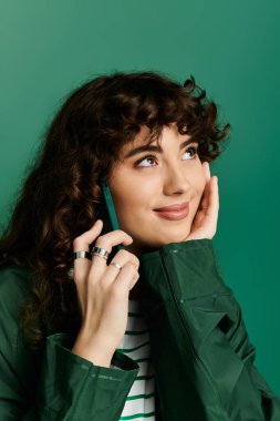 Kıvırcık saçlı ve şık yüzüklü genç bir kadın telefonunda mutlu bir şekilde sohbet ediyor, düşünceli görünüyor..