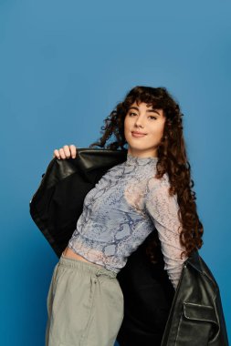 Genç bir kadın, mavi bir arkaplanda güven içinde poz verirken duygusal tarzını sergiliyor..