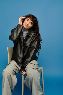 Kıvırcık saçlı modaya uygun genç bir kadın canlı mavi bir arkaplan önünde poz veriyor..