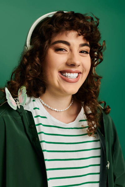 Embracing the moment, a fashionable young woman smiles joyfully against a vibrant green backdrop.
