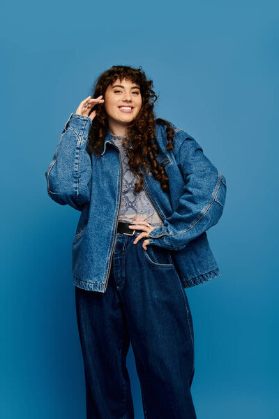Молодая женщина с вьющимися волосами моделирует свой огромный джинсовый наряд и лучи радости.